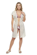 A woman modeling a cream crochet cover-up with tassel ties over a mauve bikini, standing against a solid white background.