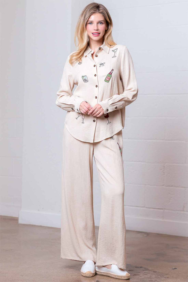 Woman wearing a beige outfit with decorative buttons against a white wall.