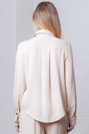 Person wearing a beige button-up shirt and pants against a light gray background
