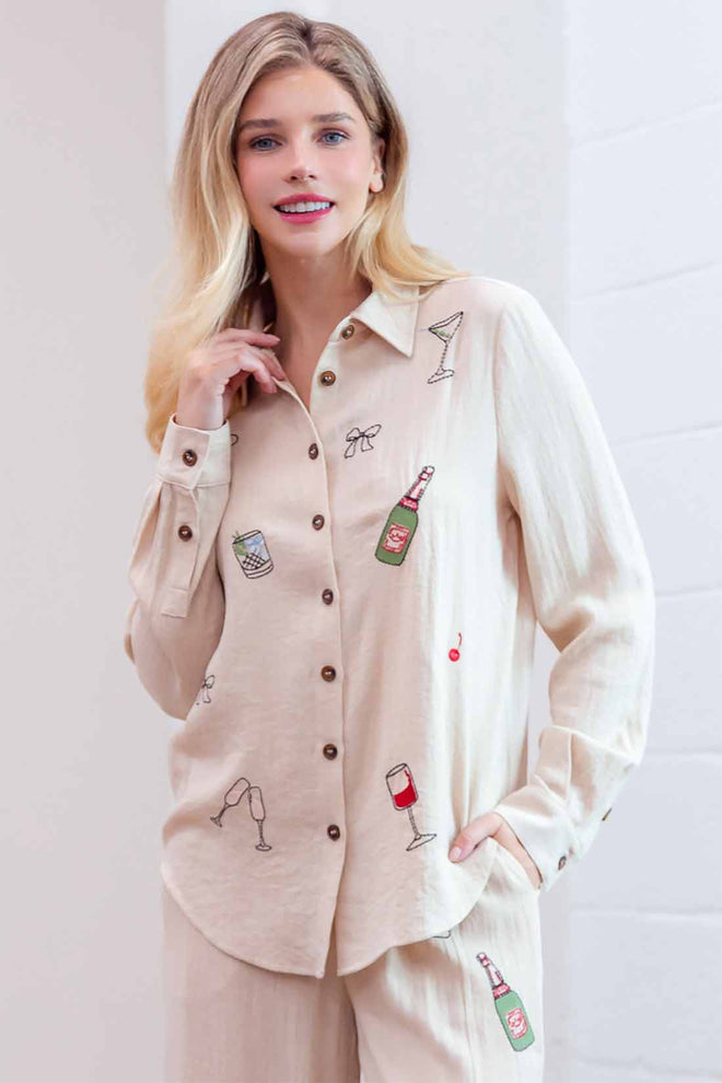 Woman wearing a beige shirt with various drink-themed embroidery on a plain background