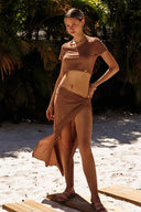 Woman in a brown outfit standing on a sandy beach with palm trees in the background